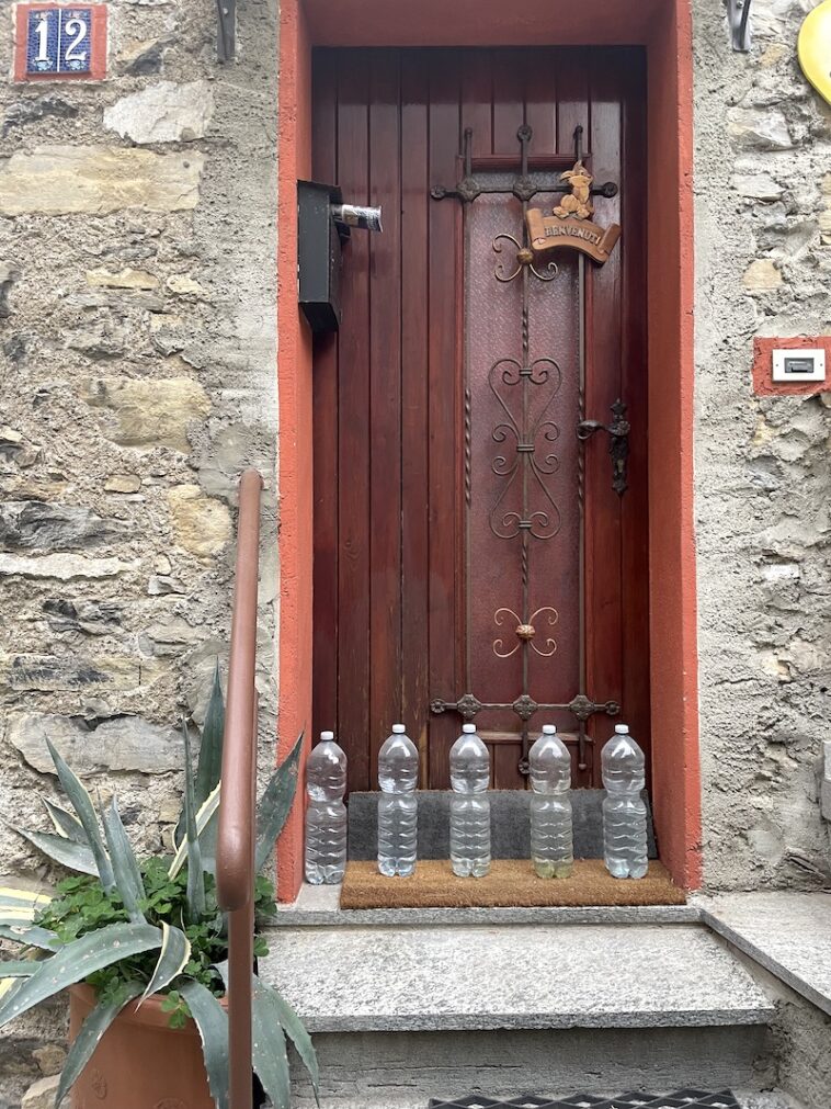 flessen water voor de deur van een huis aan het comomeer