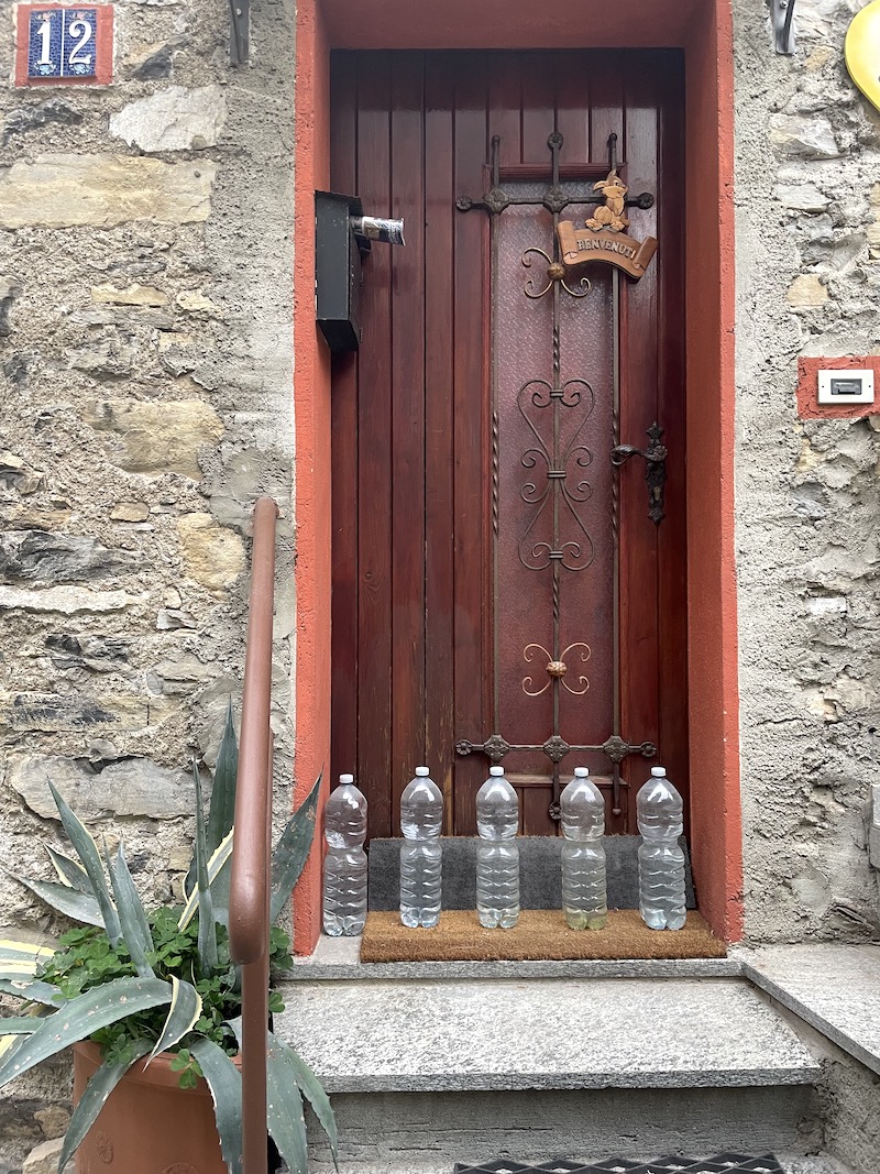 flessen water voor de deur van een huis aan het comomeer