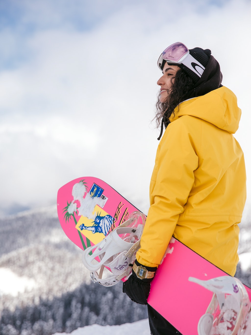 Jonge vrouw in gele jas met roze snowboard geniet van haar dure skipas in Italië